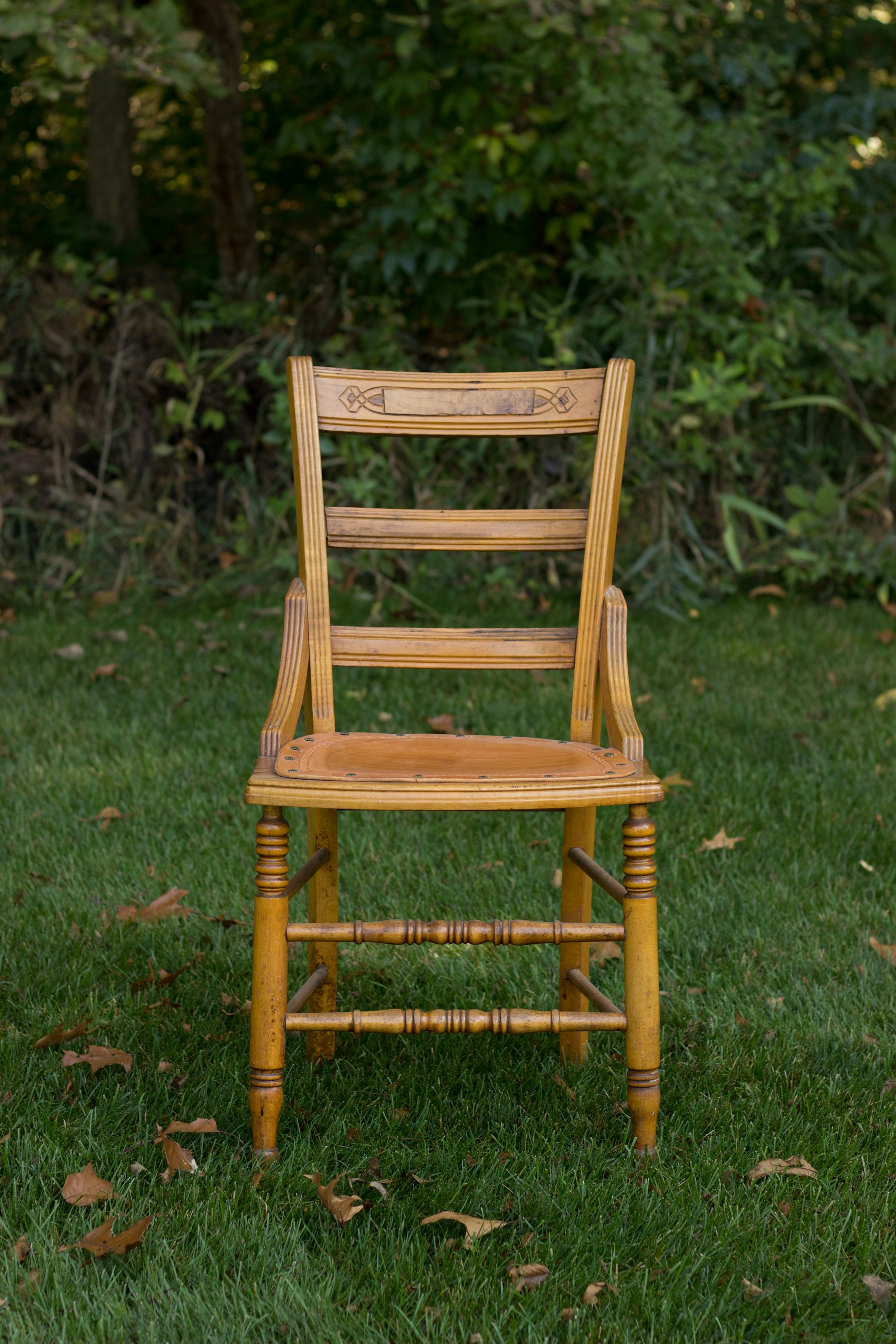 Firm wooden armchair with a straight back and armrests, standing on a clear patch of ground, no people