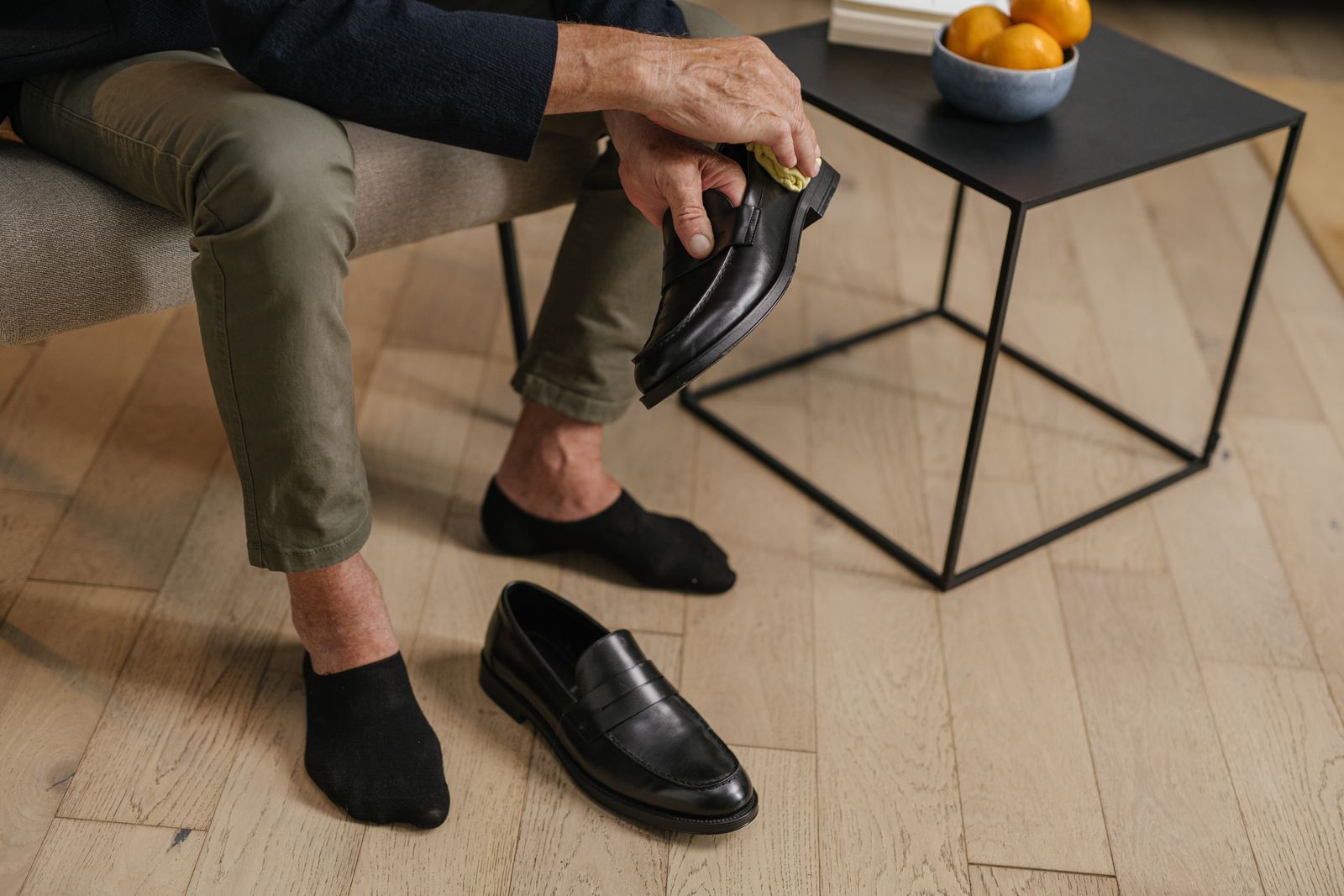 An older man seated at home holding a leather shoe in his hands, the other shoe on the floor