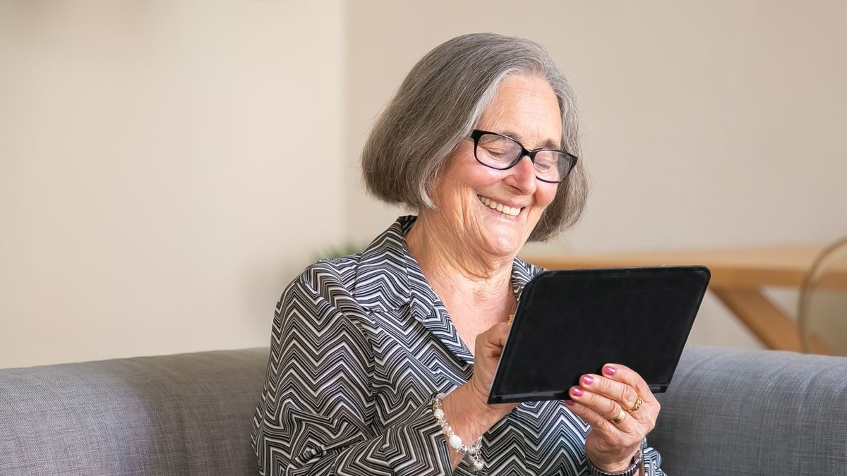 An older woman at home wearing a help-button pendant, calm and independent