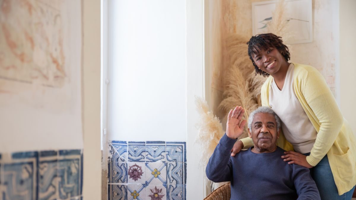 An adult daughter with her hand warmly on her elderly father's shoulder at home
