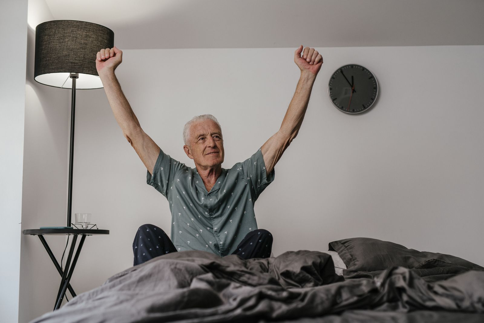 An older man waking rested and stretching in bed in the morning light